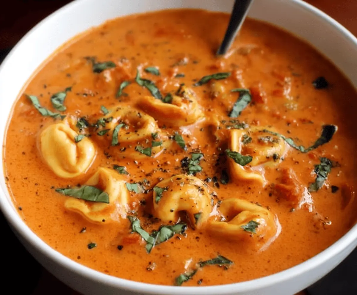 Creamy tomato basil tortellini soup in a bowl garnished with fresh basil and grated Parmesan cheese, served with crusty bread on the side.