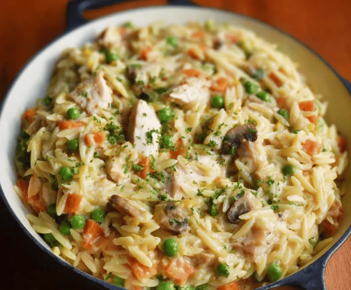 Creamy chicken pot pie orzo served in a bowl with flaky crust topping, garnished with fresh herbs, perfect for a comforting and hearty meal.