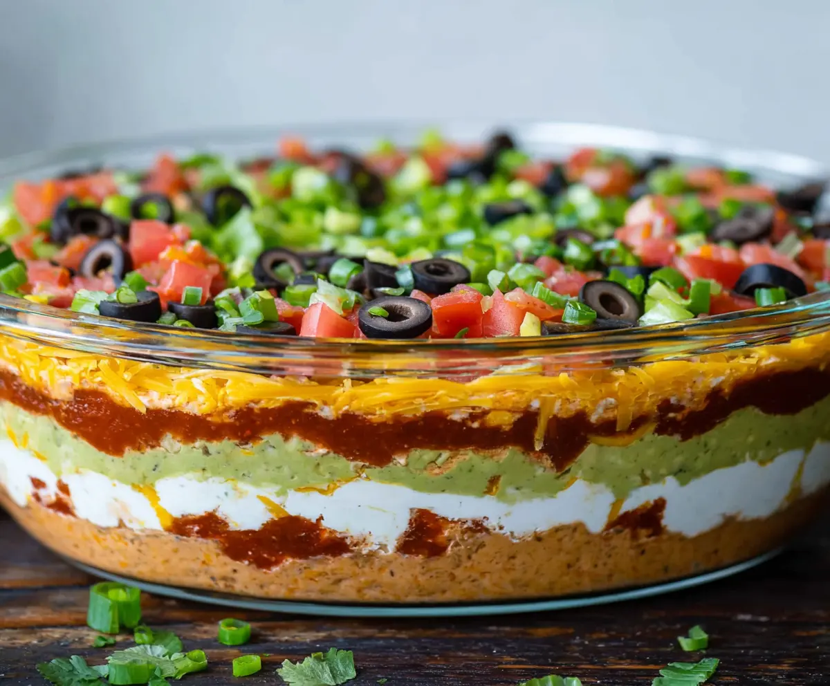 Delicious Ultimate 7 Layer Dip with vibrant ingredients including sour cream, guacamole, and salsa served in a clear bowl.